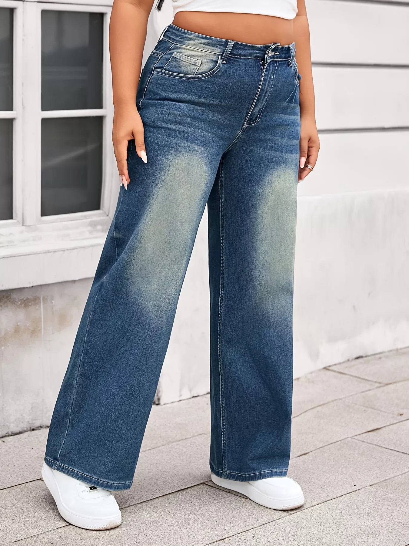 Person wearing blue wide-leg jeans and white sneakers on a sidewalk.