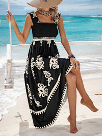 Woman in a black dress with white patterns sitting on a swing by the beach.