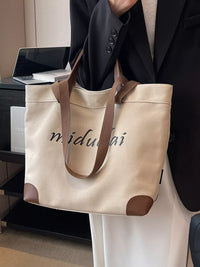 Person holding a beige tote bag with brown handles and accents, featuring the brand 'midu'.