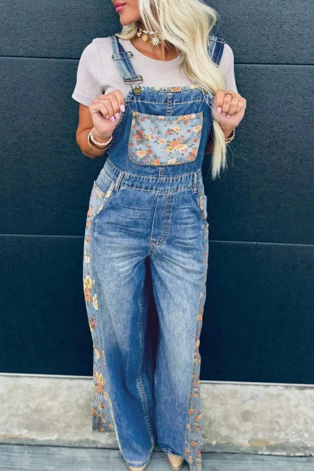 Person wearing floral denim overalls against a blue wall