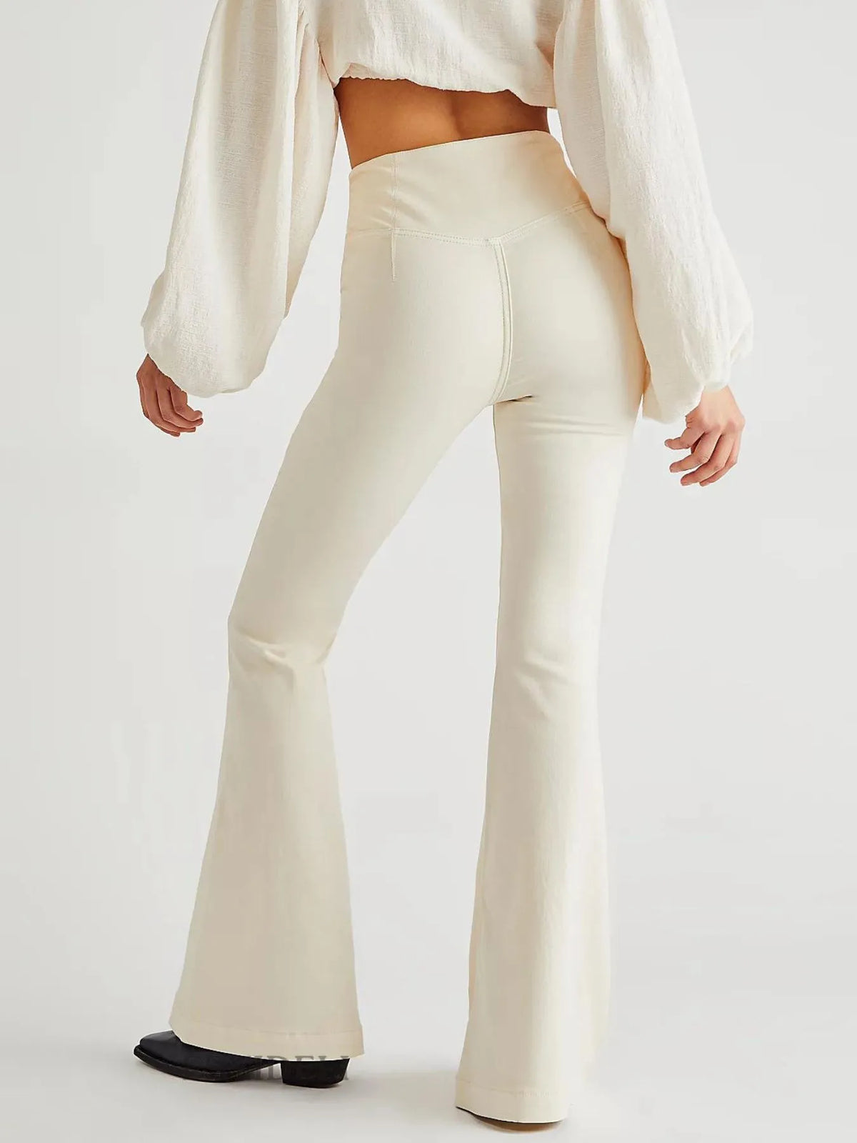 Person wearing a white blouse and cream-colored flared pants on a light gray background