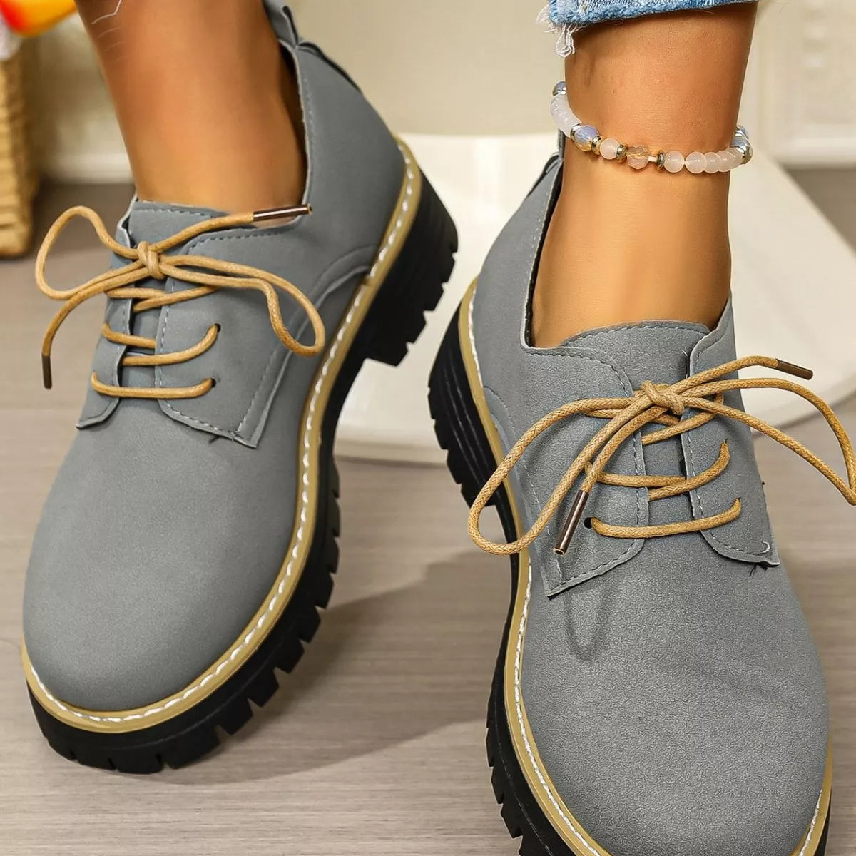 Gray shoes with brown laces worn by a person on a wooden floor.