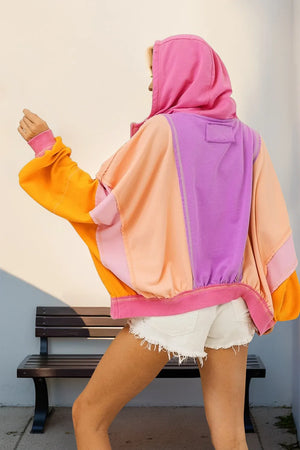 Person wearing a colorful hoodie with pink, orange, and purple sections, sitting on a bench.