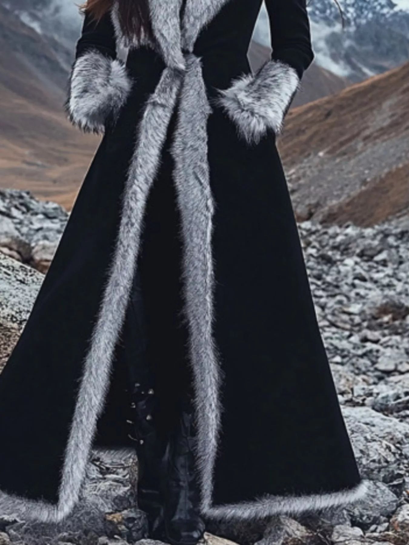 Person wearing a long black coat with fur trim in a mountainous landscape