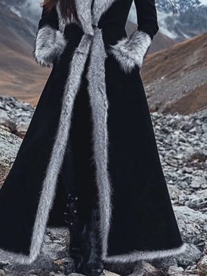 Person wearing a long black coat with fur trim in a mountainous landscape