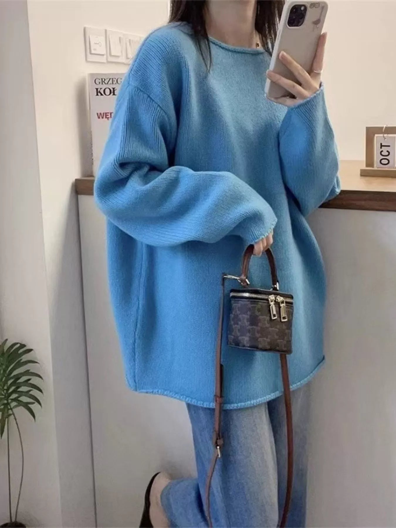 Person wearing a blue sweater holding a handbag indoors.