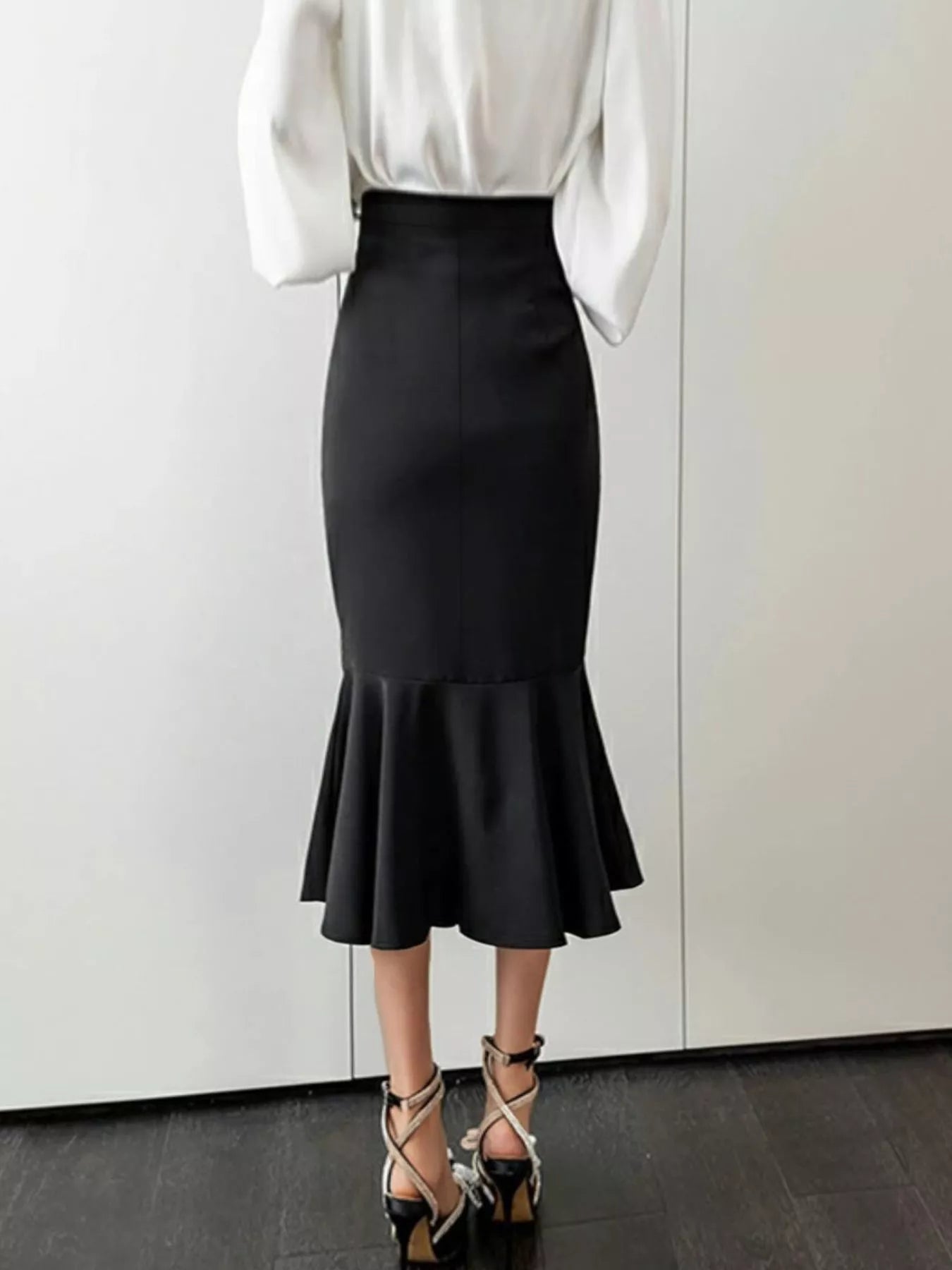 Person wearing a black ruffled skirt and white blouse against a plain background