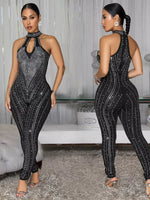 Woman wearing a black sequin jumpsuit in a room with a couch and decorative items.