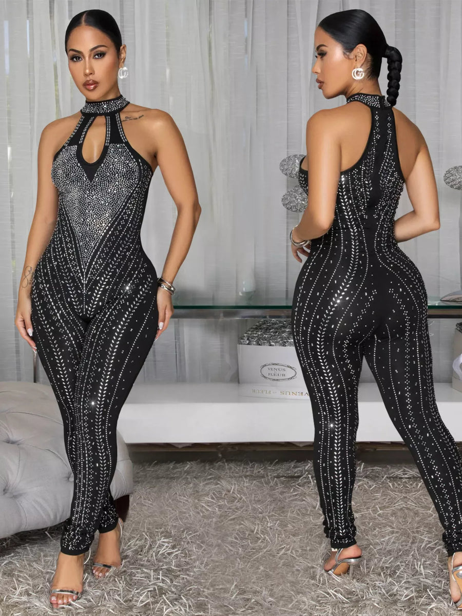 Woman wearing a black sequin jumpsuit in a room with a couch and decorative items.