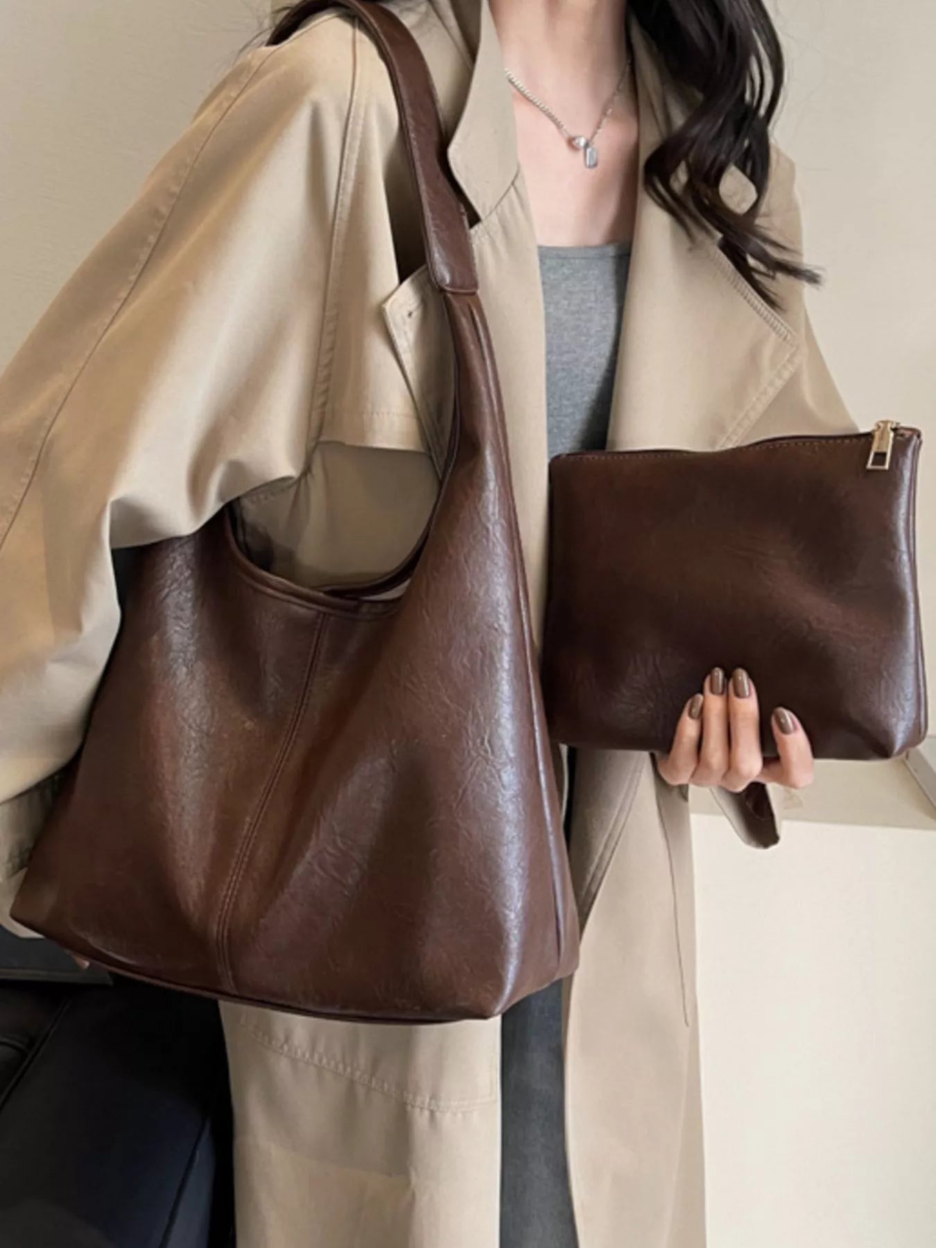 Person holding a brown leather handbag and matching clutch.