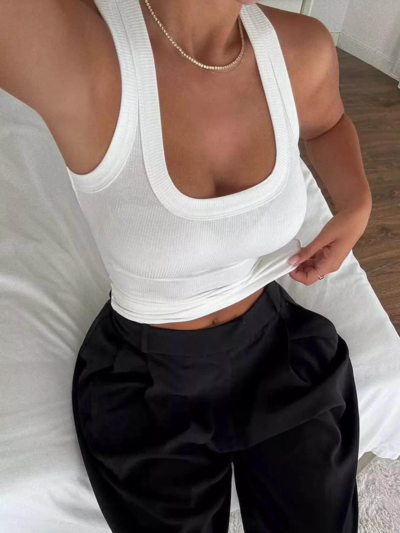 Person wearing a white tank top and black pants on a bed.