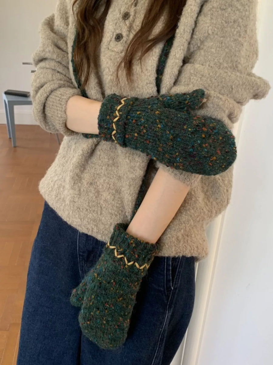 Person wearing green knitted mittens and a beige cardigan indoors.