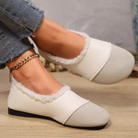 White loafers with fluffy trim worn by a person on a wooden floor.