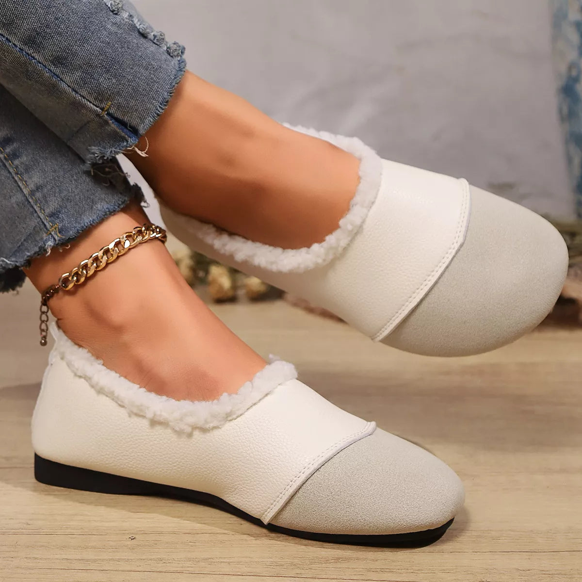 White loafers with fluffy trim worn by a person on a wooden floor.