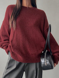Person wearing a maroon sweater holding a black handbag against a neutral background