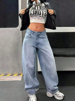 Person wearing a black jacket, white crop top with text, and blue jeans standing in front of a train.