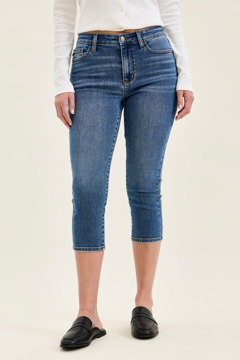 Person wearing blue jeans and a white top on a beige background