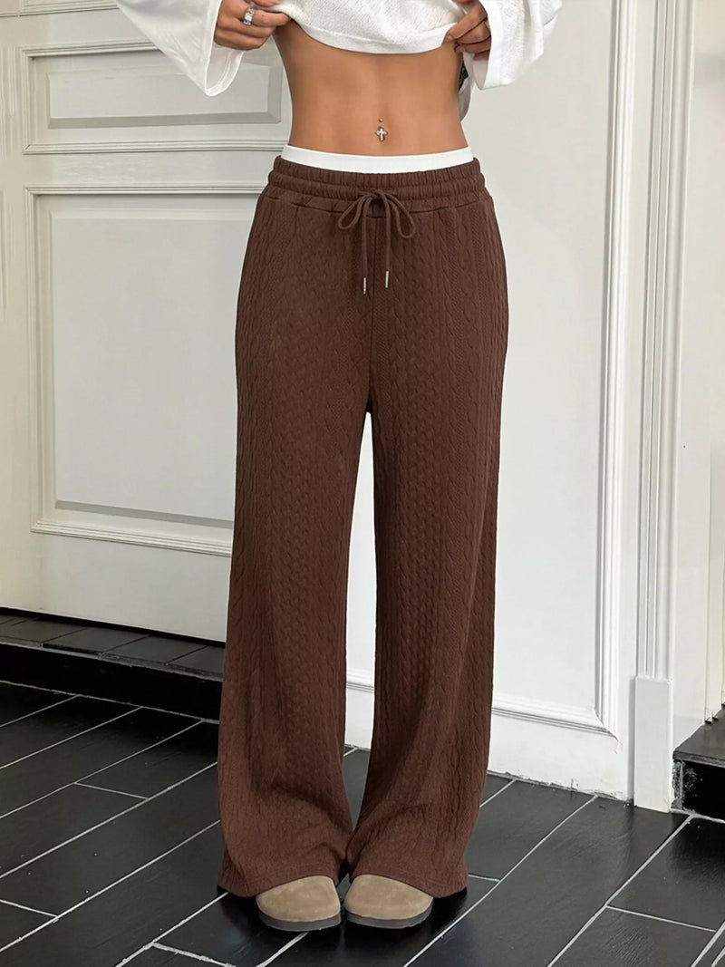 Person wearing brown wide-leg pants and a white top in a room with a white door.