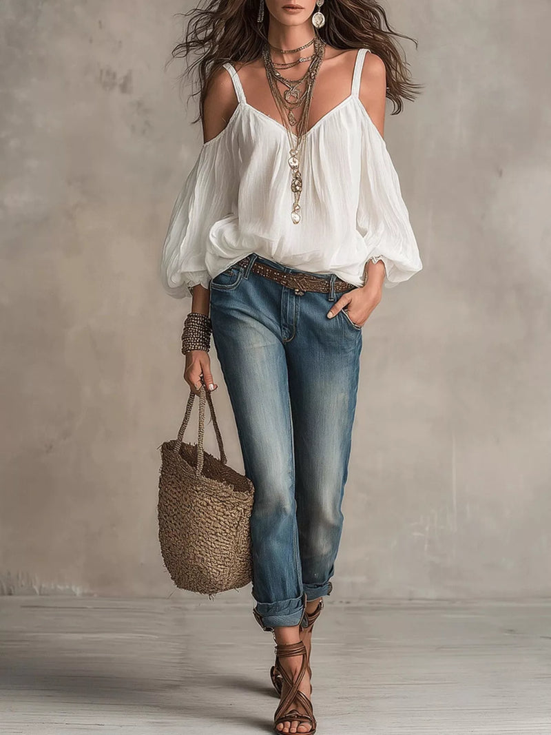 Woman wearing a white blouse, blue jeans, and holding a straw bag against a neutral background