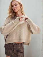 Woman wearing a beige sweater and brown pants against a light gray background