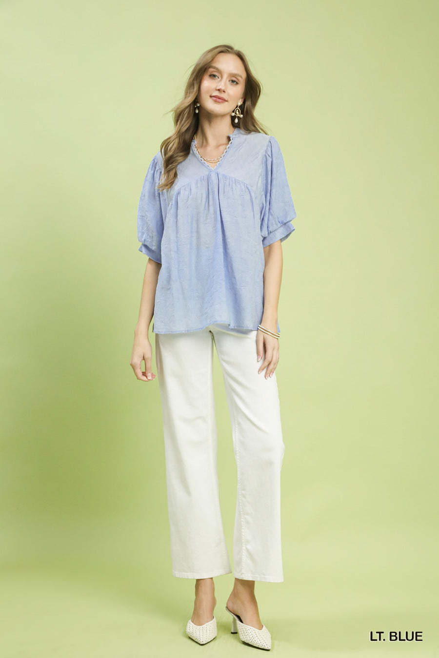 Woman wearing a light blue blouse and white pants on a green background