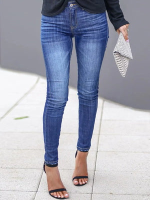 Person wearing blue jeans and black sandals on a sidewalk.