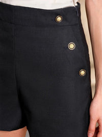 Black shorts with gold buttons on a neutral background