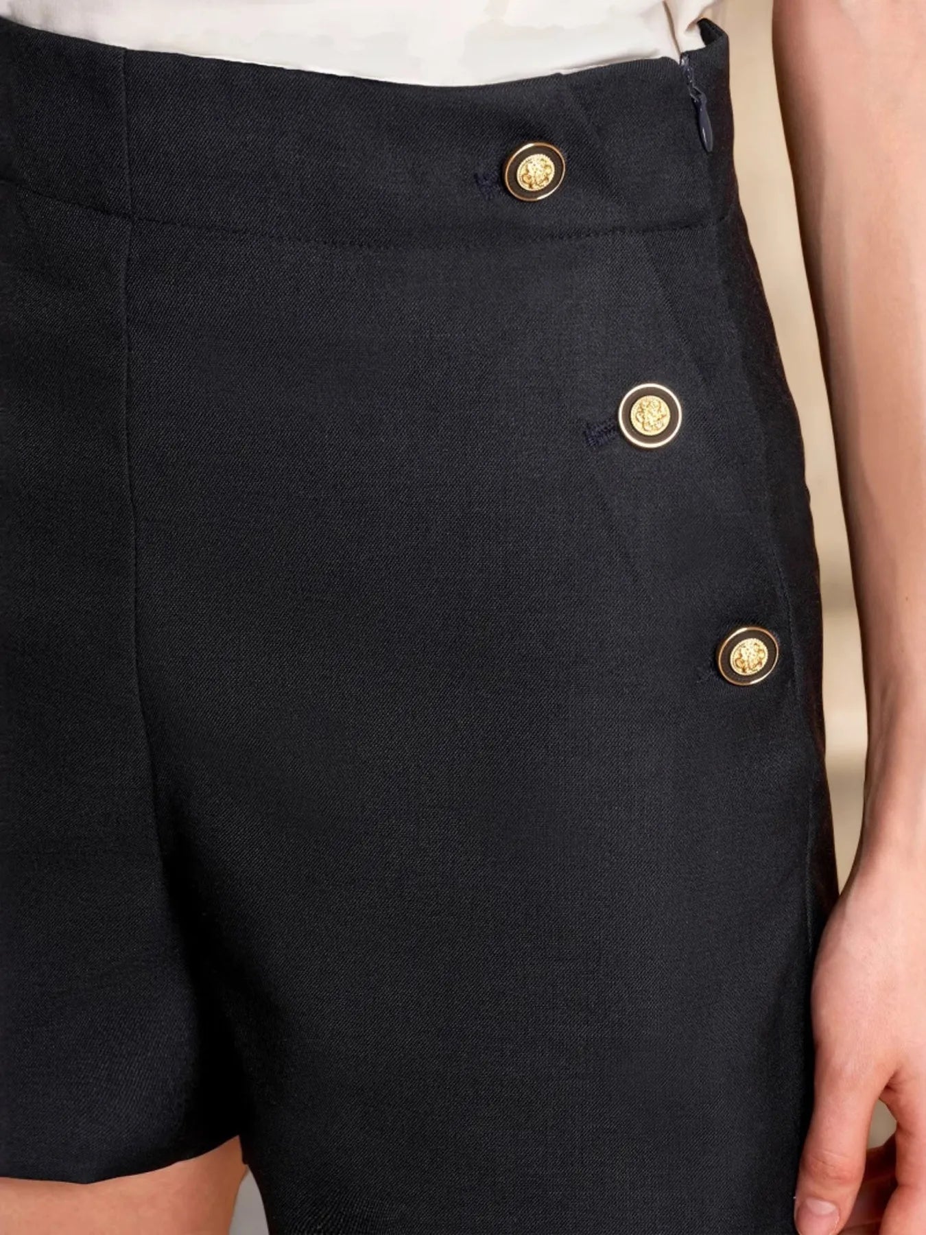 Black shorts with gold buttons on a neutral background