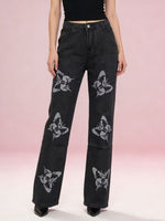 Black jeans with butterfly patterns worn by a person on a pink gradient background