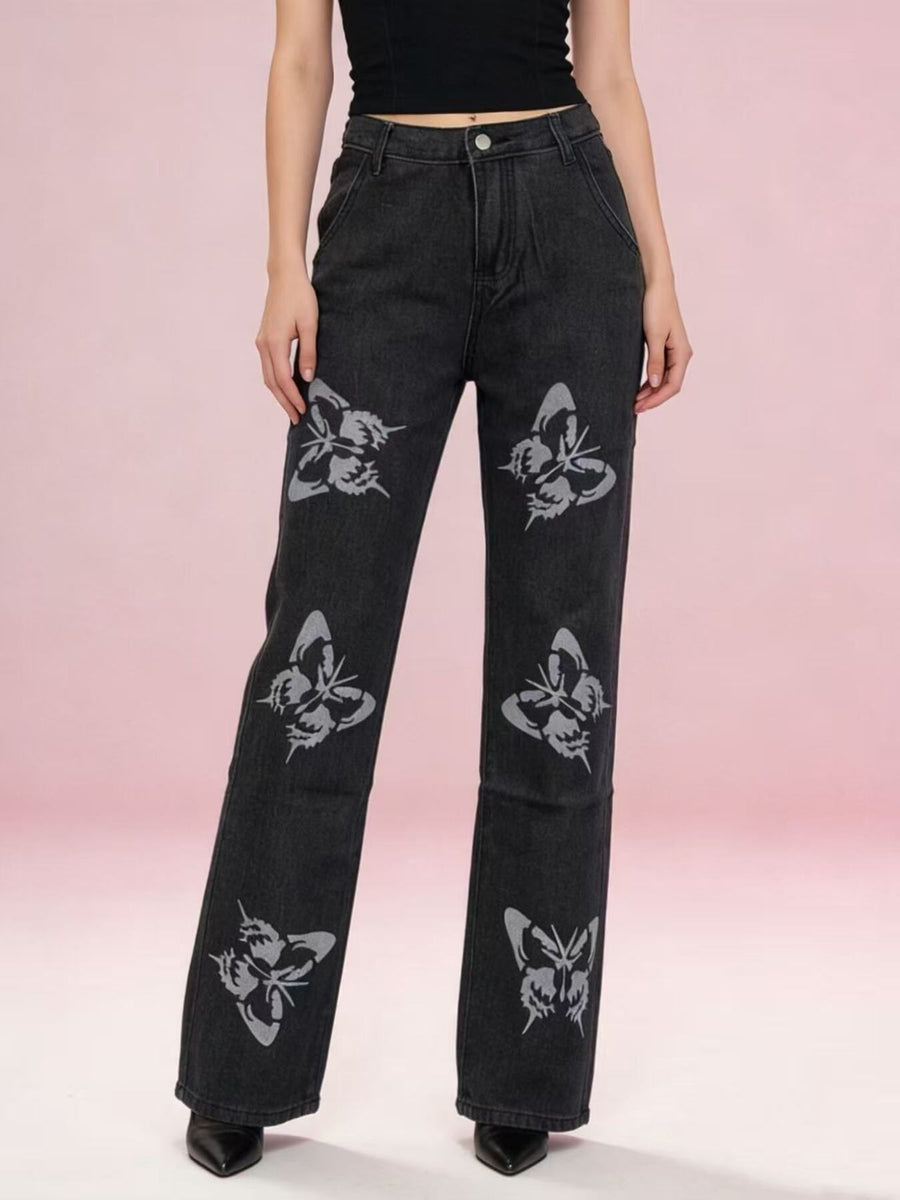 Black jeans with butterfly patterns worn by a person on a pink gradient background