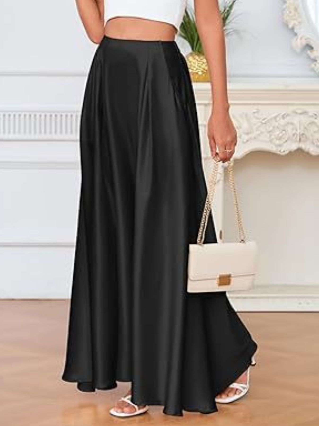 Person wearing a black skirt and white top, holding a beige handbag indoors.