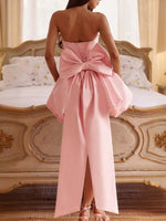 Pink strapless gown with a large bow detail in front of an ornate bed.