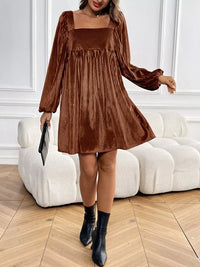 Woman wearing a brown pleated dress with long sleeves in an indoor setting.
