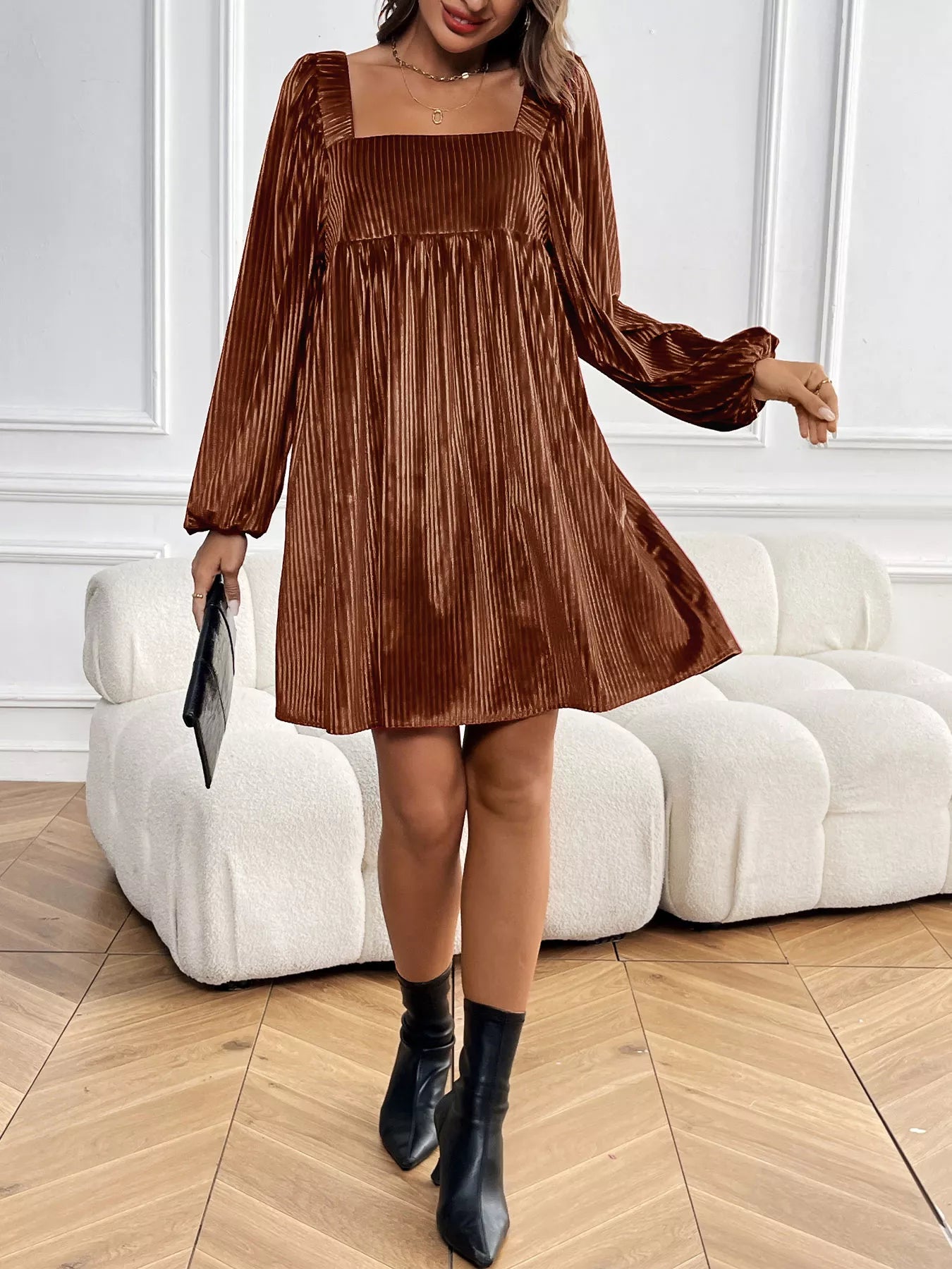 Woman wearing a brown pleated dress with long sleeves in an indoor setting.