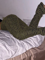 A person lying on a bed wearing olive green fuzzy striped knit pants and matching socks in a bedroom setting.