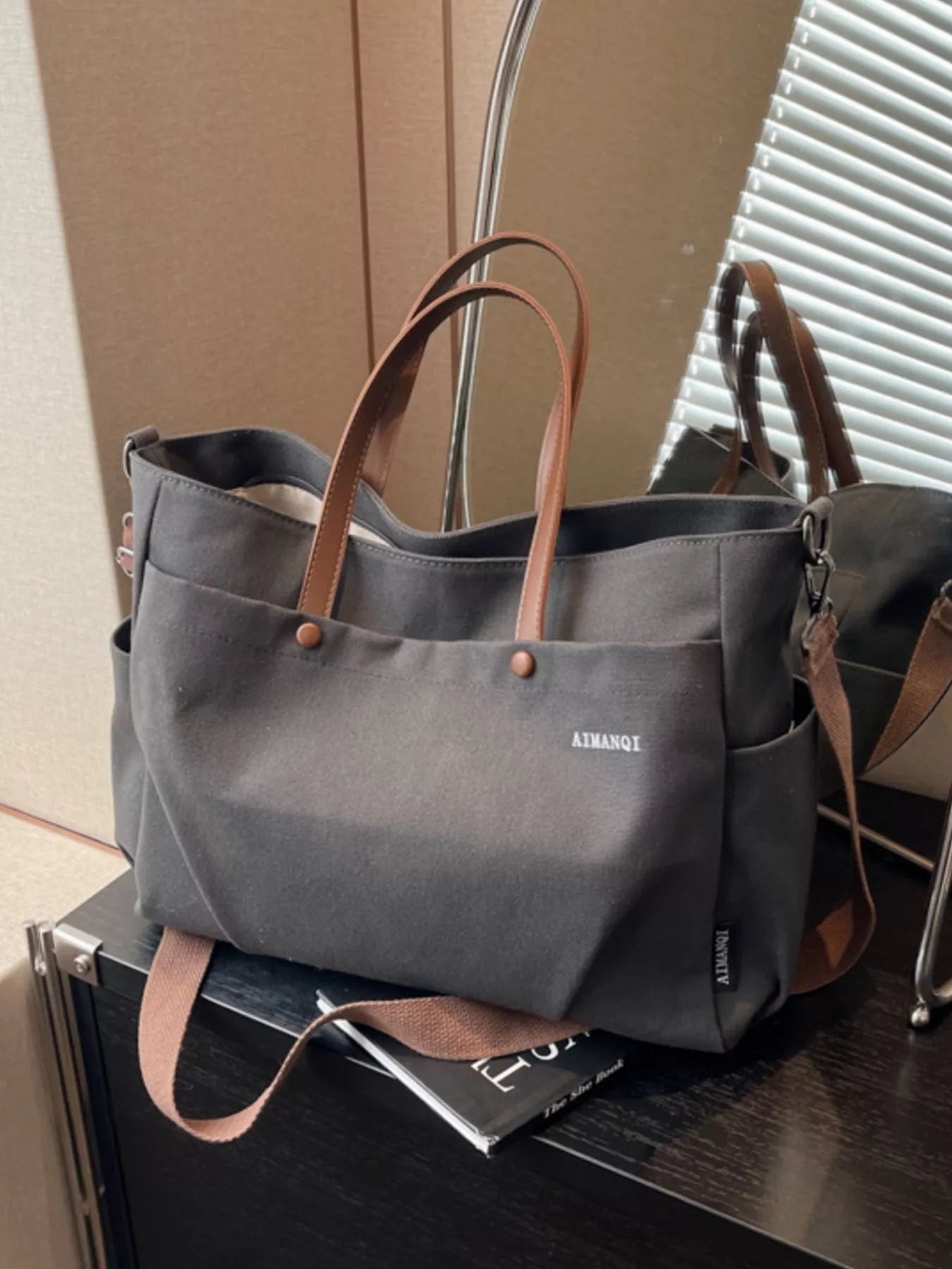 Gray tote bag with brown handles on a surface