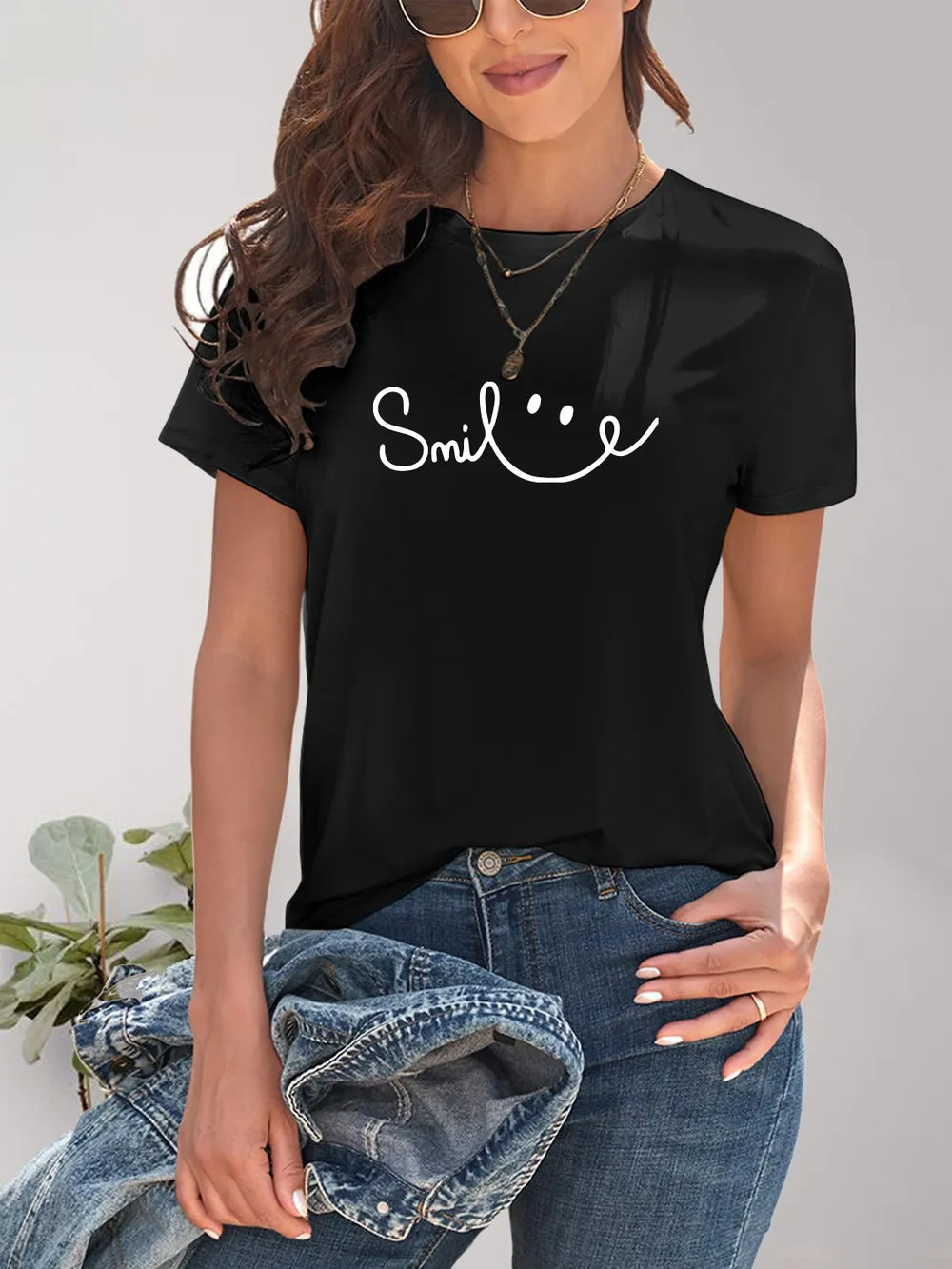Person wearing a black t-shirt with 'Smile' text, holding a denim jacket.