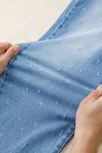 Close-up of hands holding a piece of blue denim fabric with white stitching details.