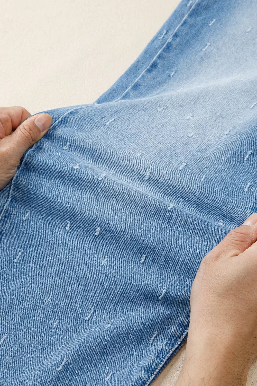 Close-up of hands holding a piece of blue denim fabric with white stitching details.