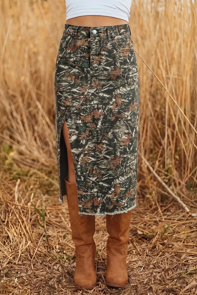 A person wearing a camouflage midi skirt with a side slit, paired with brown suede boots, standing in a field of dry grass.
