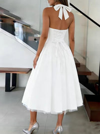 Woman wearing a white halter neck dress with a bow detail in an indoor setting.