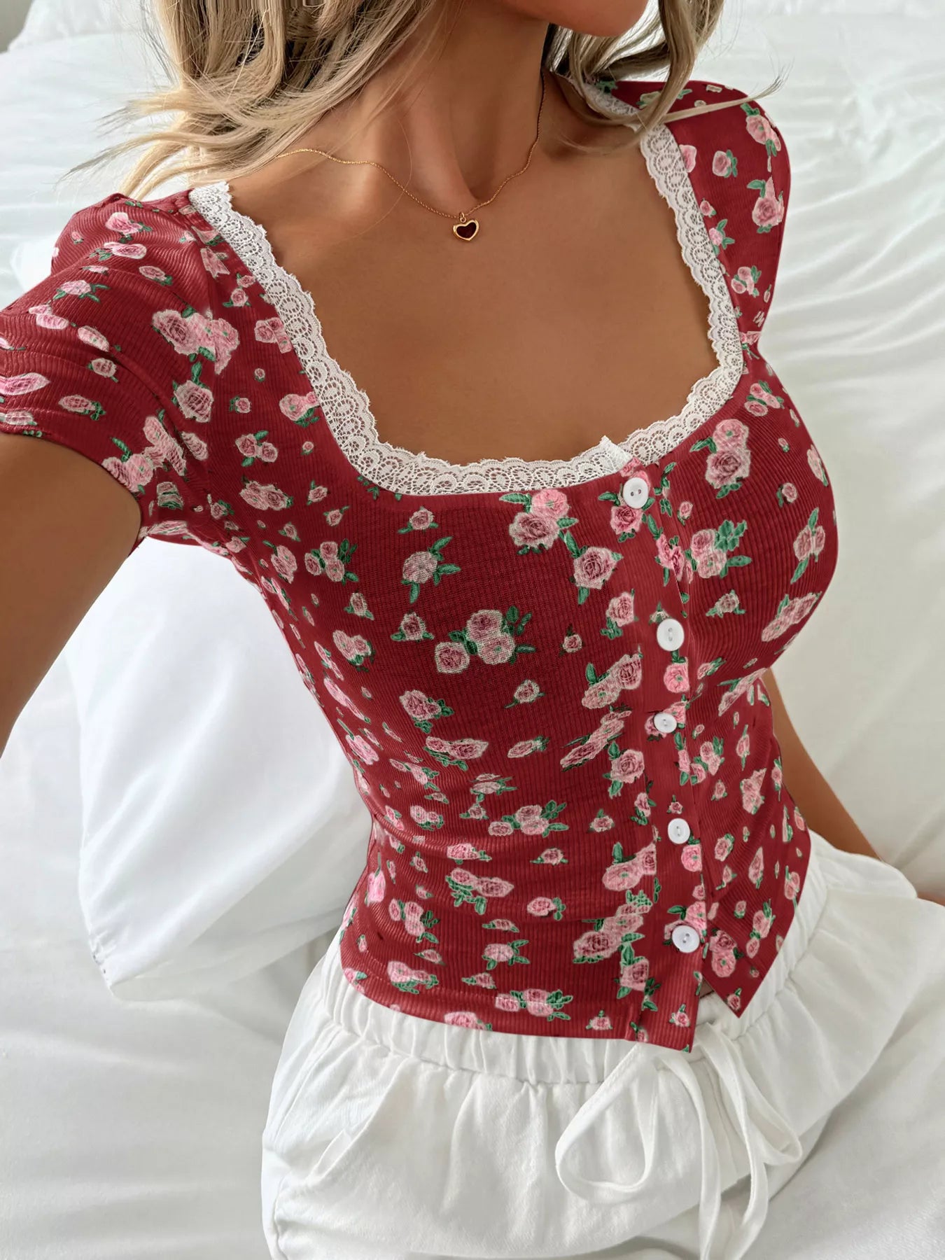 Red floral top with white lace trim worn by a person on a white background