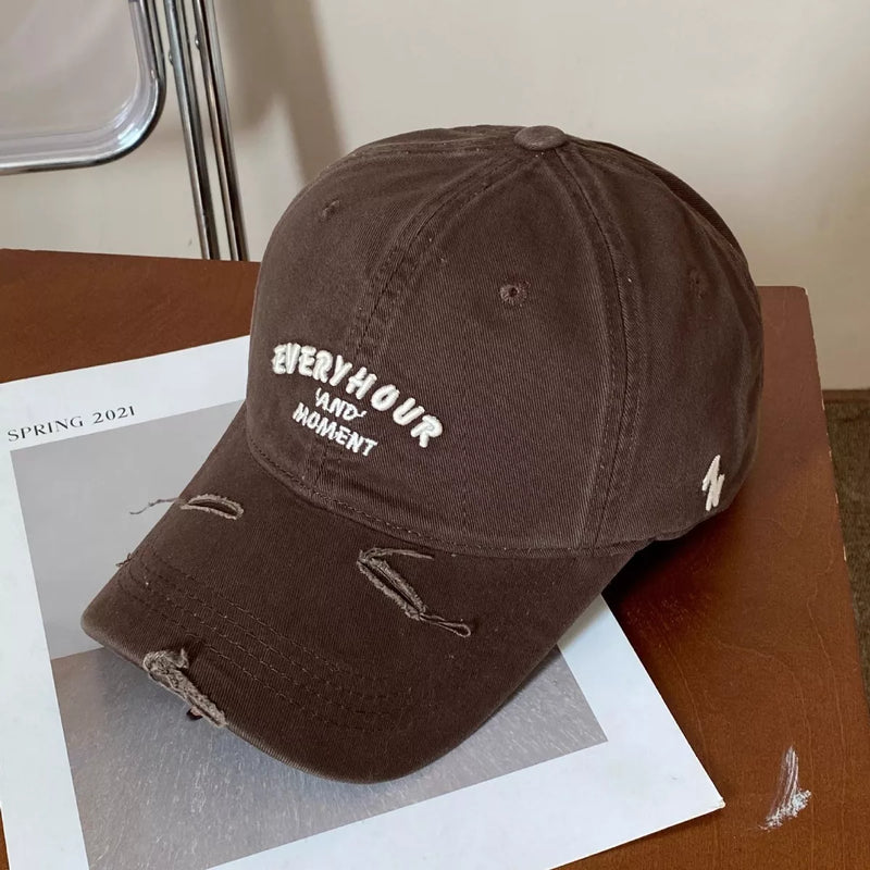Brown distressed baseball cap with white text on a wooden surface with a magazine underneath.