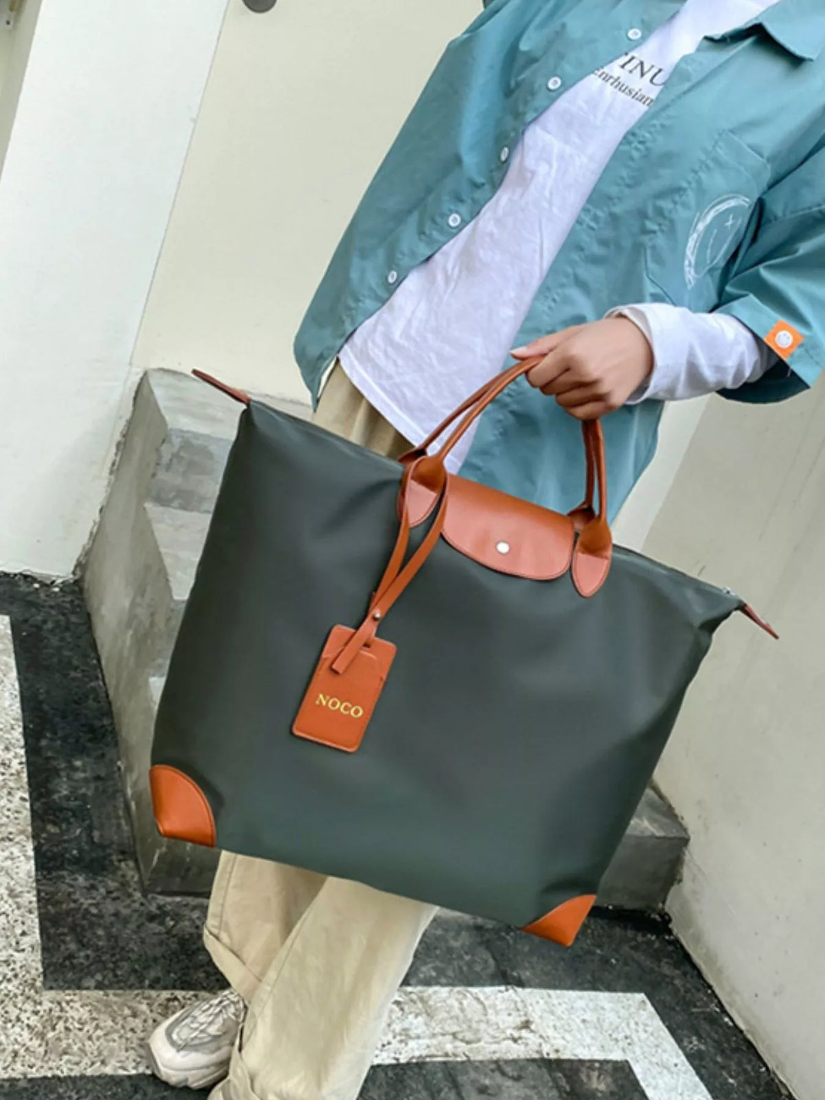 Person holding a green and brown bag with a visible brand tag, standing on steps.