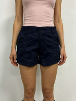 Person wearing navy shorts and a light pink top on a plain background