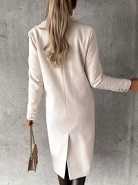 Person wearing a beige coat against a gray concrete wall