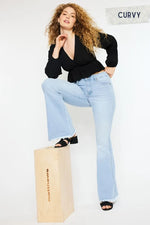 Woman wearing light blue jeans and a black top sitting on a wooden box with 'Curvy' text in the corner.