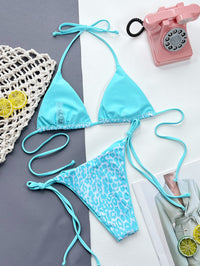 Blue bikini set with leopard print bottom on a gray and white background with a pink phone and lemon slices.