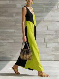 Woman wearing a black and green dress holding a handbag against a stone wall background