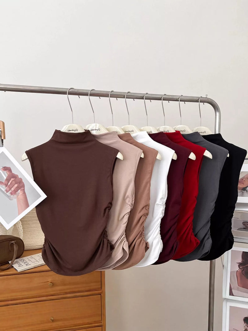 Row of sleeveless tops in various colors hanging on a rack against a neutral wall.